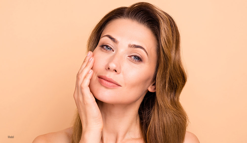 a beautiful woman with light brown hair and flawless skin holds a hand up to her face